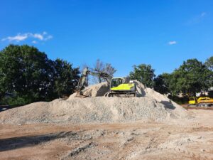 Excavator working on a gravel pile at an outdoor construction site with clear blue sky.